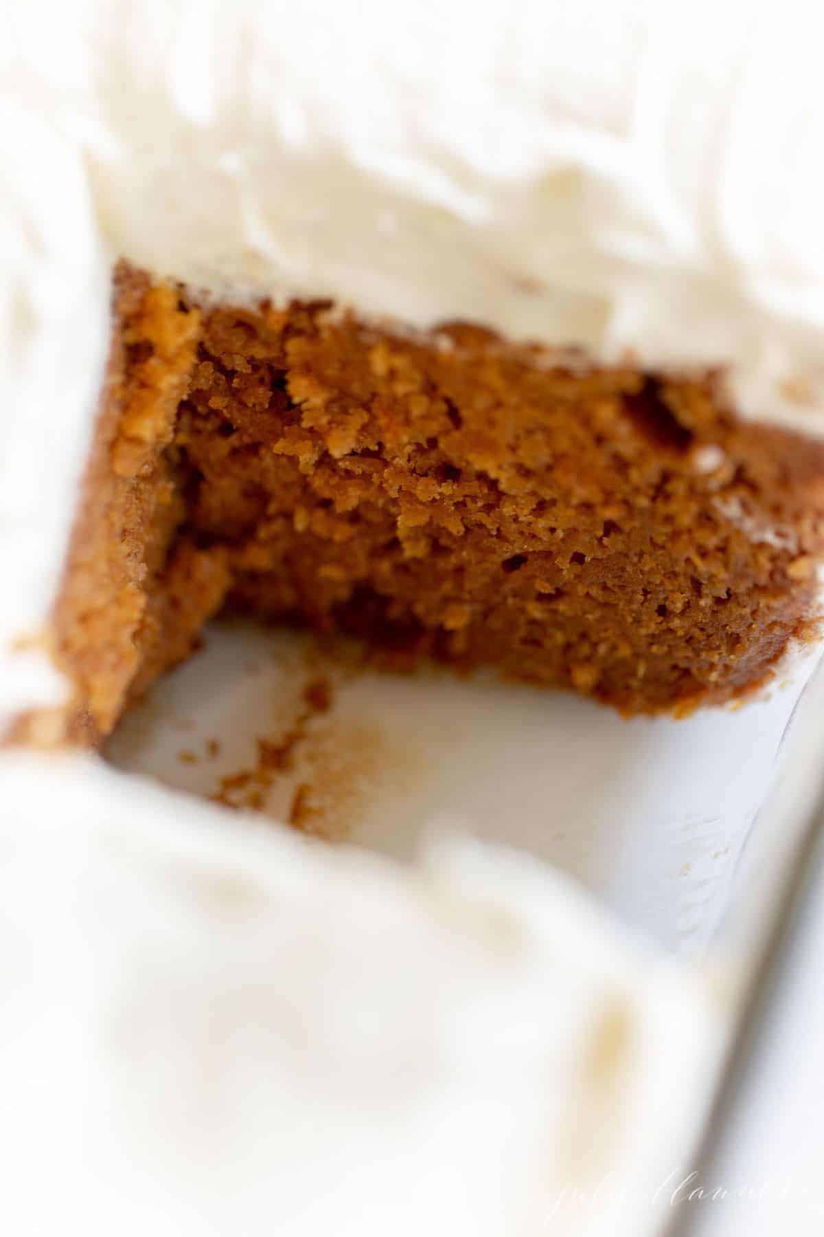 Pumpkin cake frosted with cream cheese frosting on a marble surface, with a piece missing.