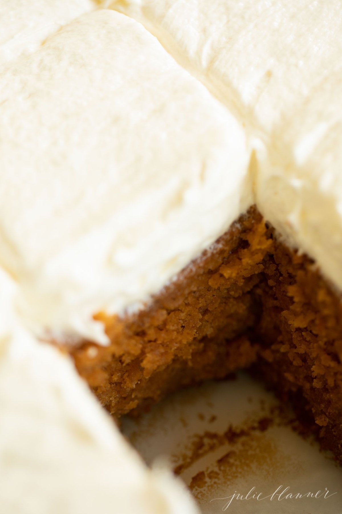 A pumpkin cake recipe topped with fluffy cream cheese frosting, with one slice cut out.
