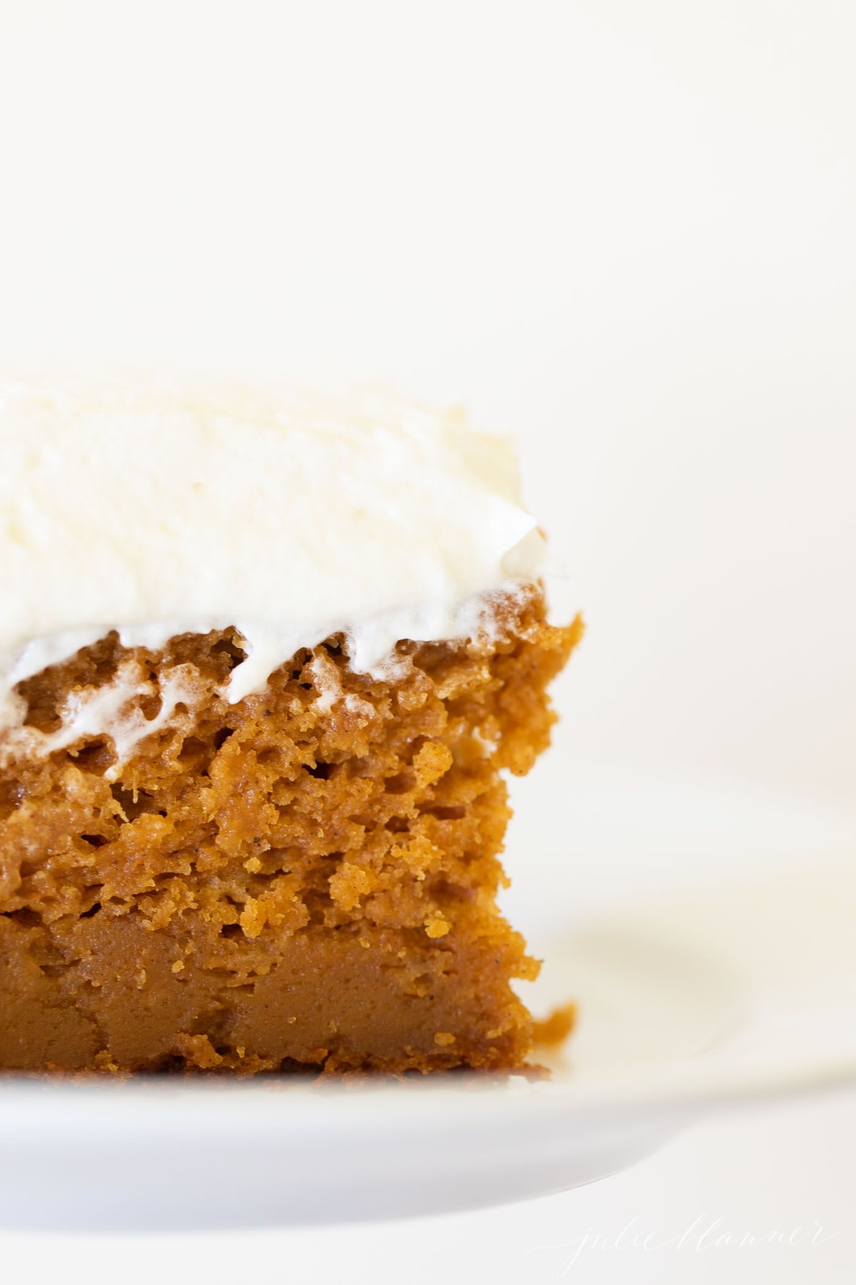 A slice of pumpkin cake with a thick layer of cream cheese frosting on a white plate.