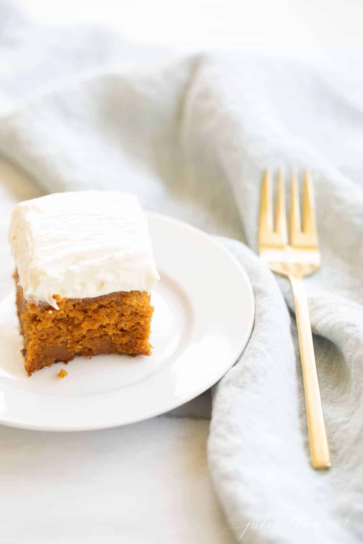A slice of pumpkin cake on a white plate. Blue linen napkin and gold fork to the side.