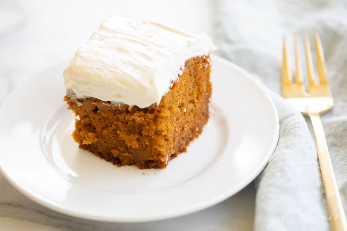 Cut pumpkin bars iced with cream cheese frosting on a white plate on a marble surface. 