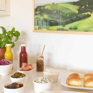 Burger toppings displayed in white ceramic bowls, condiments in rear and buns to the side. #burgerbar #burgershop #sliderbar