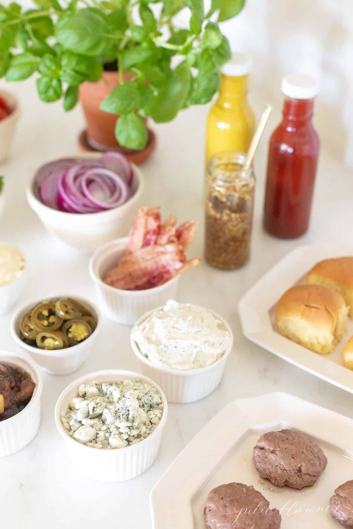 Burger toppings displayed in white ceramic bowls, condiments in rear and buns to the side. #burgerbar #burgershop #sliderbar