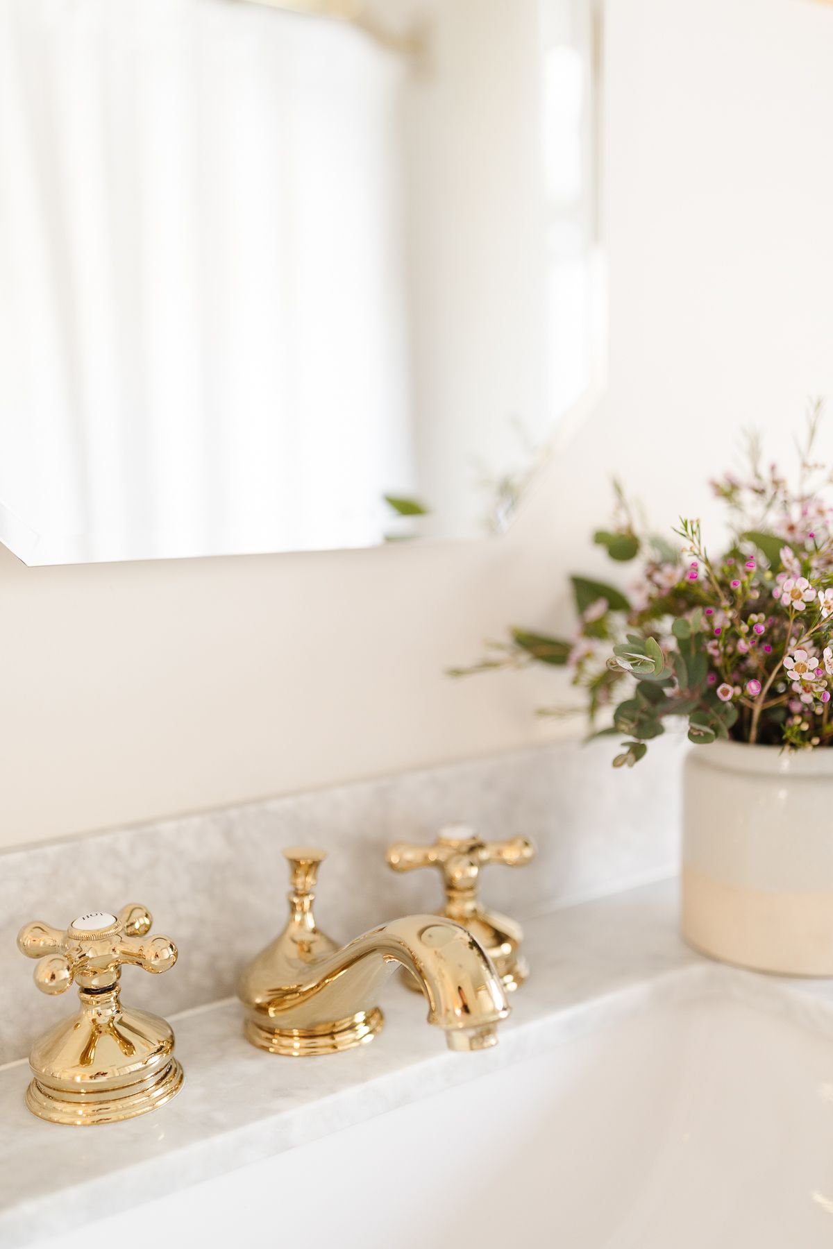 A gold faucet on a marble topped vanity with flowers in the background