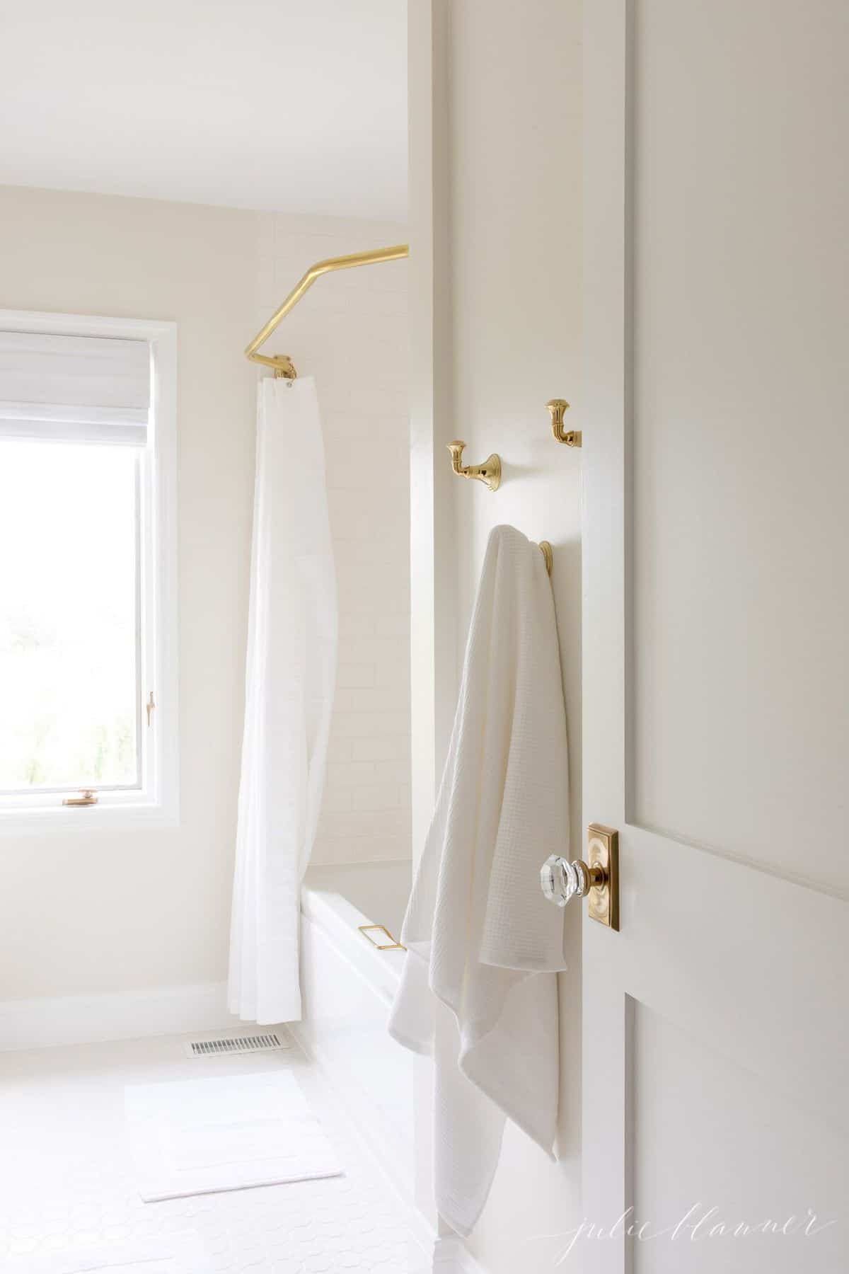 A white bathroom shot featuring brass towel hooks and a brass shower curtain rod.