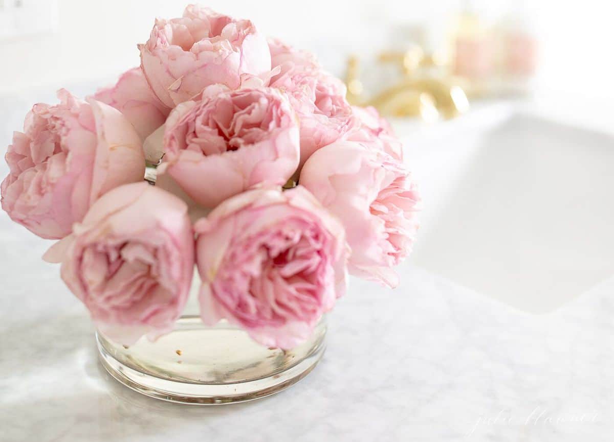 Blush pink garden roses in a clear vase resting on a marble vanity top. #spabath #showerniche
