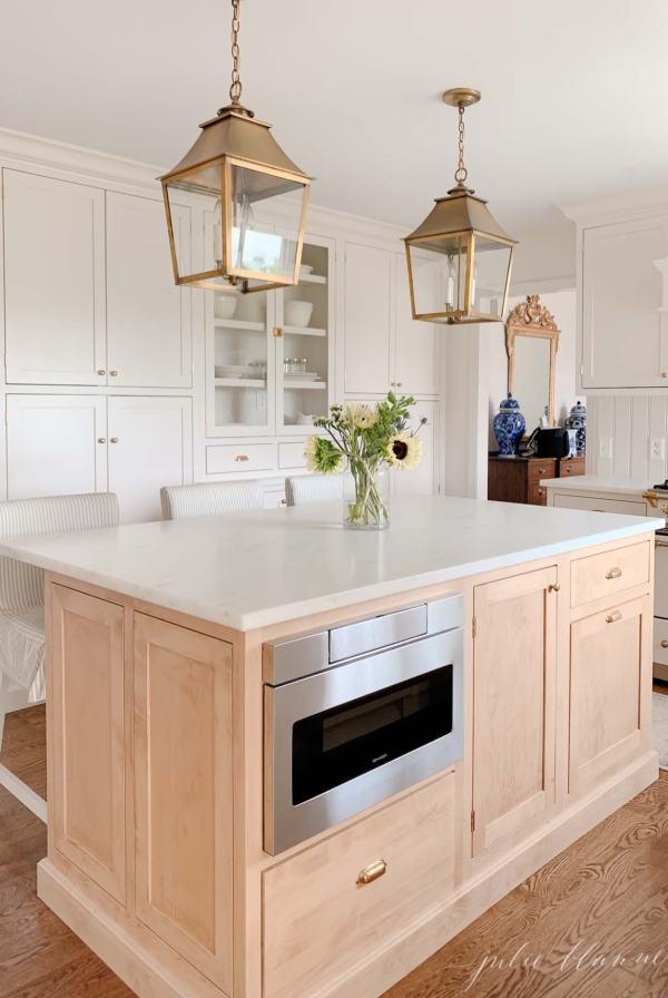 A classic kitchen with cream cabinets, brass hardware and brass lanterns and an under counter microwave drawer.