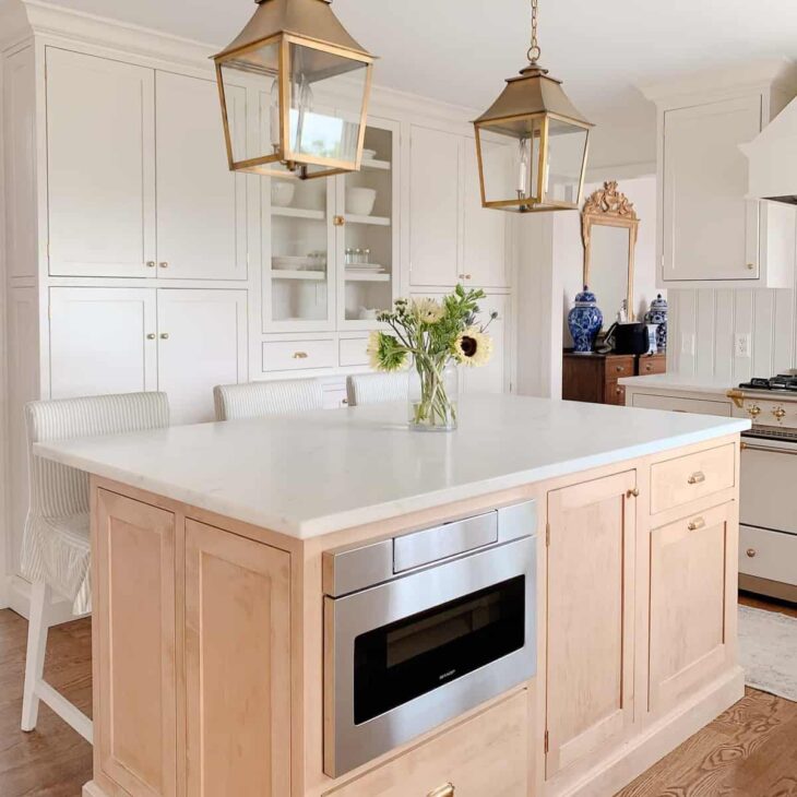 A classic kitchen with cream cabinets, brass hardware and brass lanterns and an under counter microwave drawer.