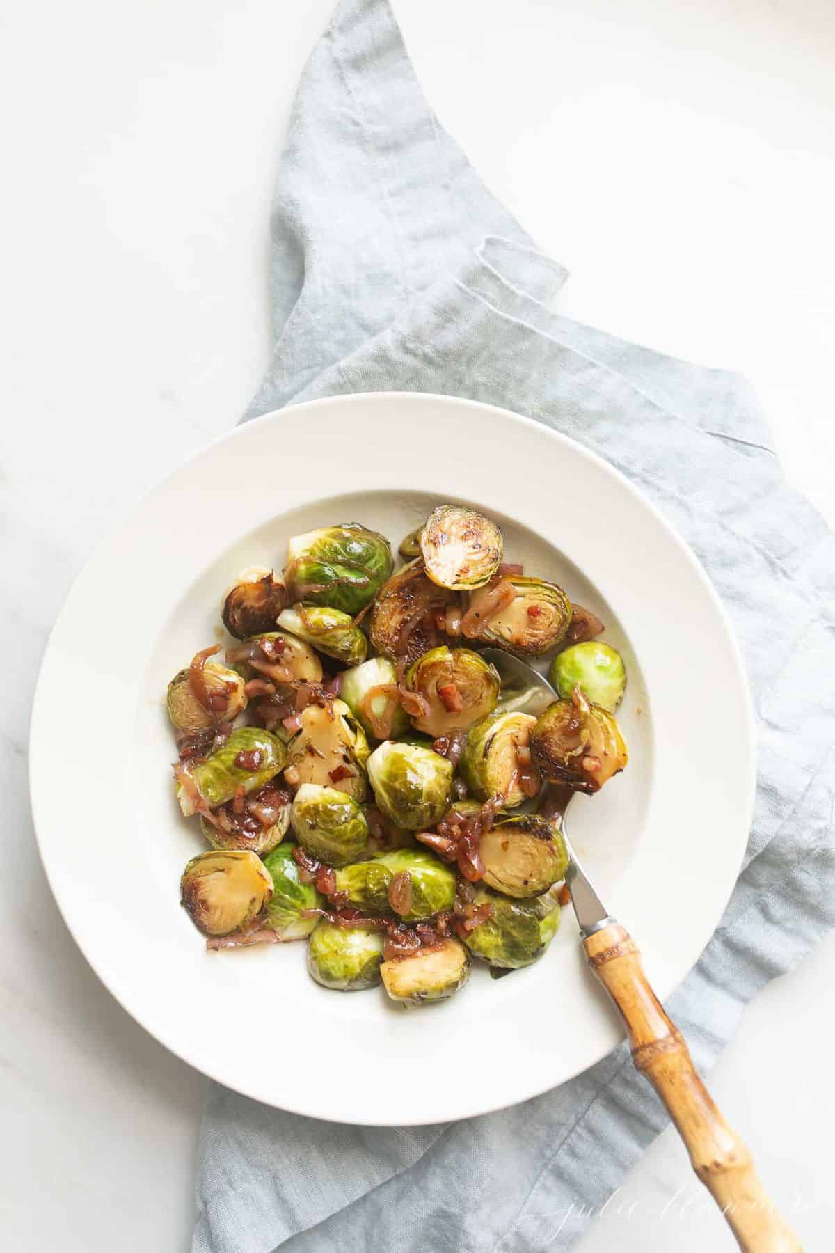 White bowl with sauteed brussel sprouts, blue linen napkin to the side.