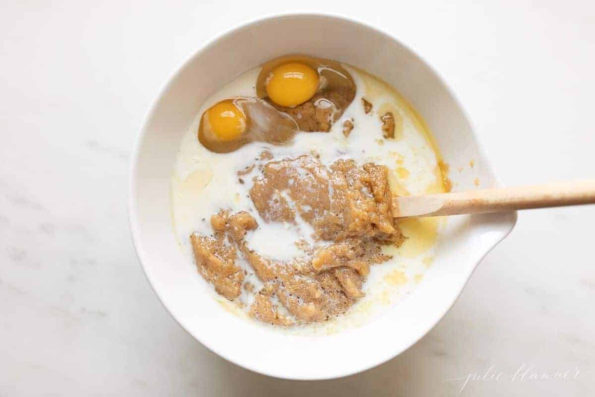 Eggs mixed into a batter in a white mixing bowl, wooden spoon insde.