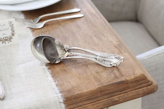 Wooden farm table, antique silver serving utensils on the edge.