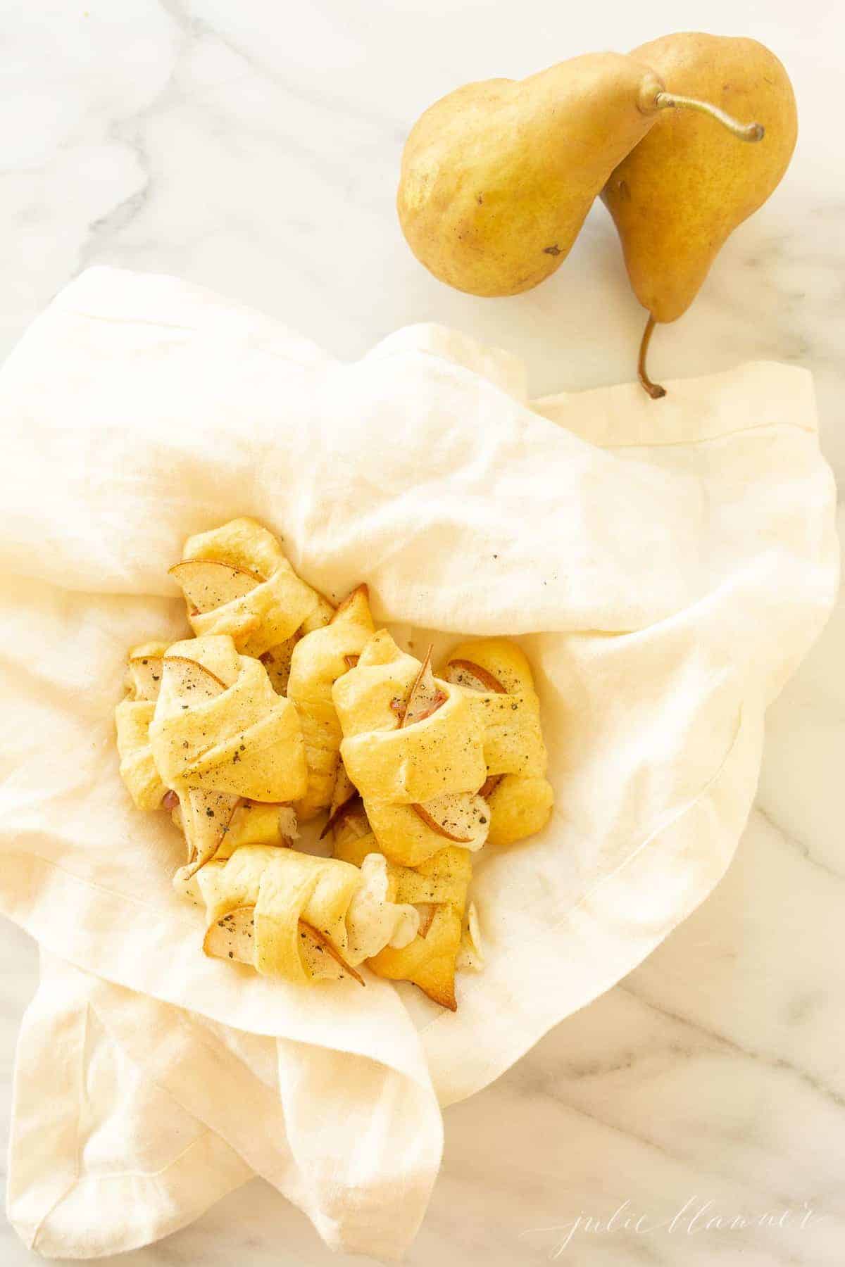 cresecent roll appetizer in a linen lined bowl with pears next to it