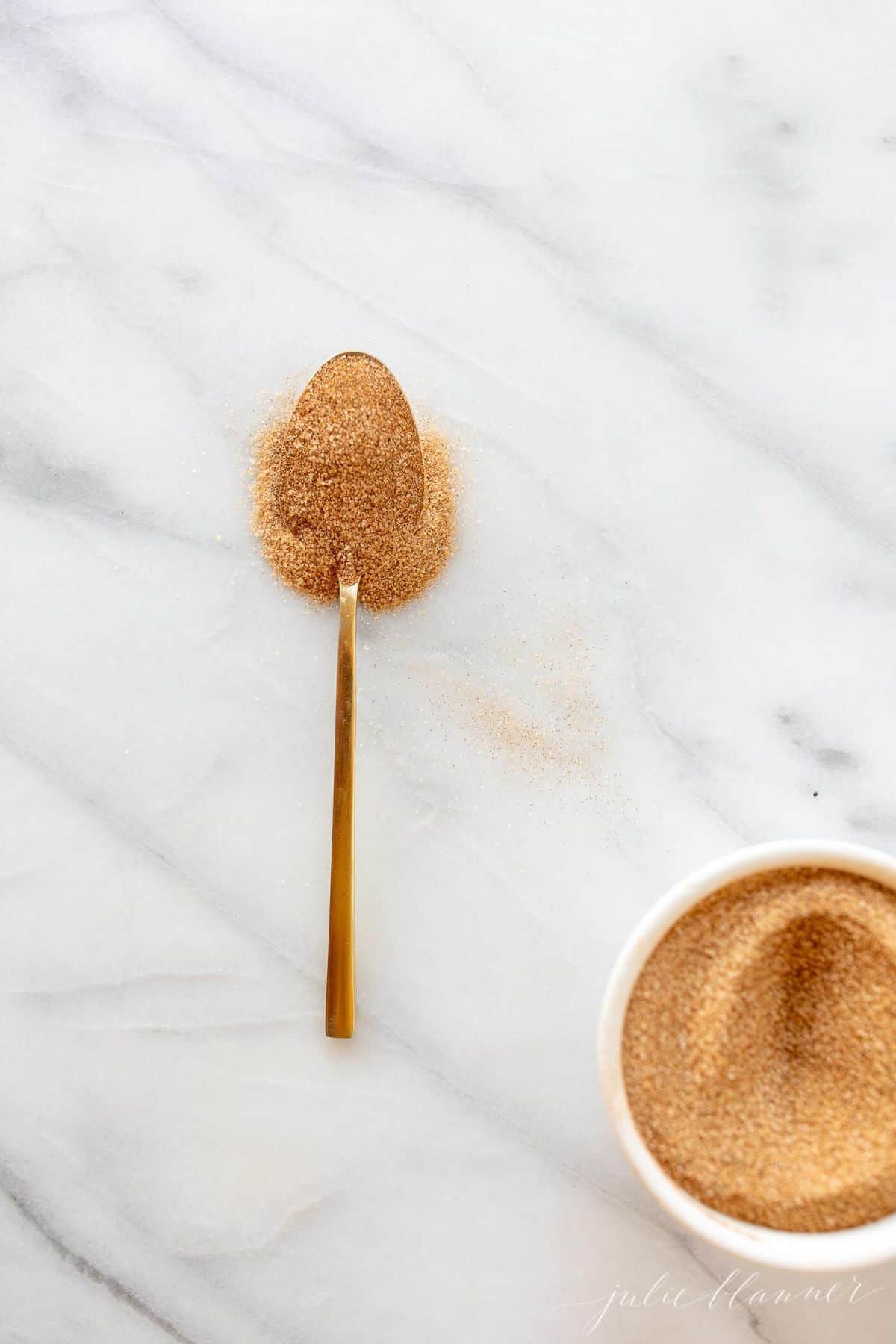 White marble surface, gold spoonful of cinnamon sugar recipe messy on the counter.