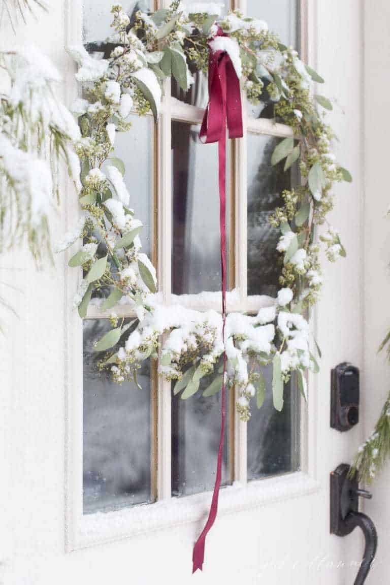 Glass paned exterior door decorated with a Christmas wreath, fresh snow on the wreath.