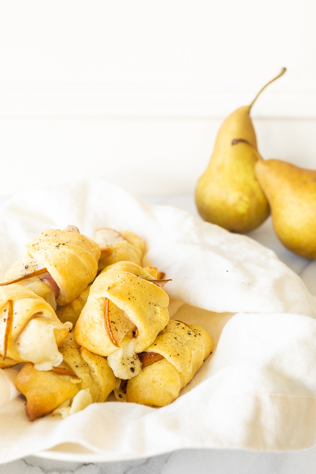 A plate with pears, a napkin, and crescent roll appetizers next to it.