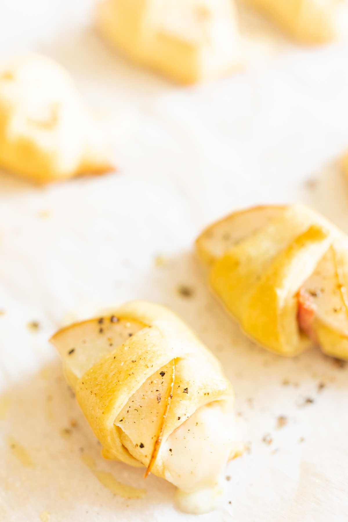 A sheet of parchment paper with a bunch of apple wrapped Crescent Roll Appetizers on it.