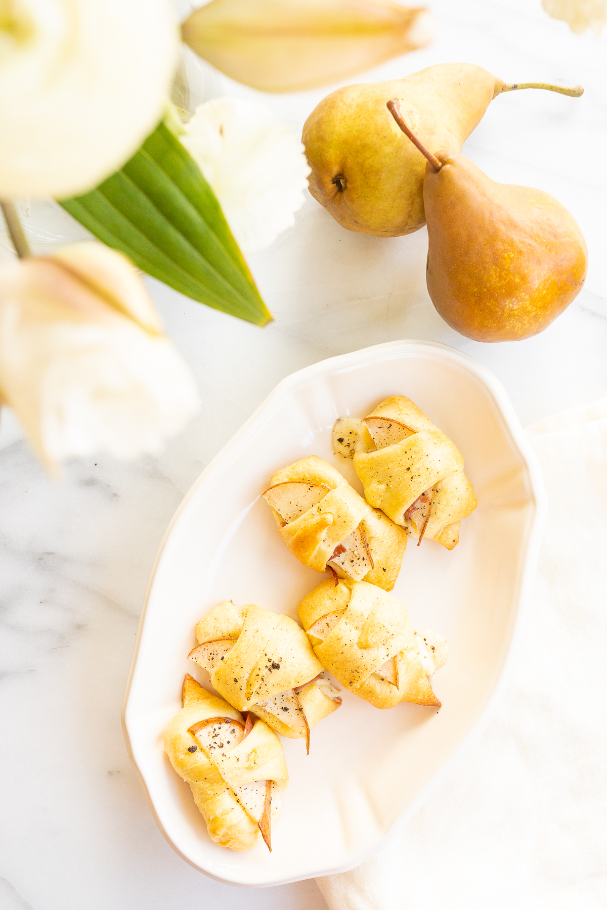 A plate with pears and flowers on it, accompanied by mouthwatering crescent roll appetizers.