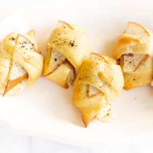 A white plate with a plate of stuffed apples wrapped in crescent rolls.
