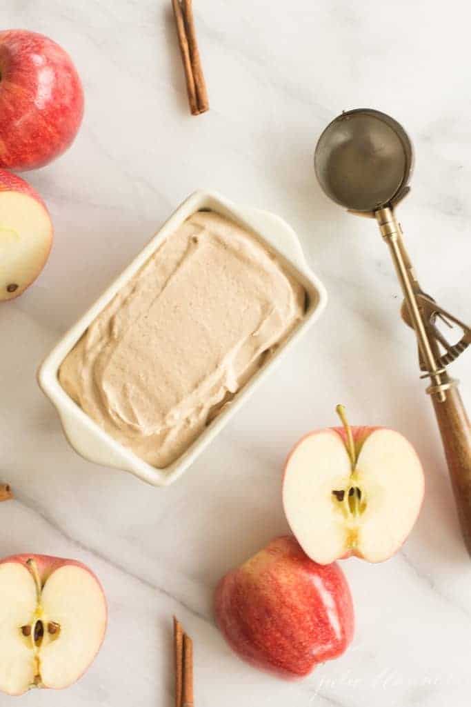 Marble surface with a dish of apple ice cream- ice cream scoop and sliced apples to the side.