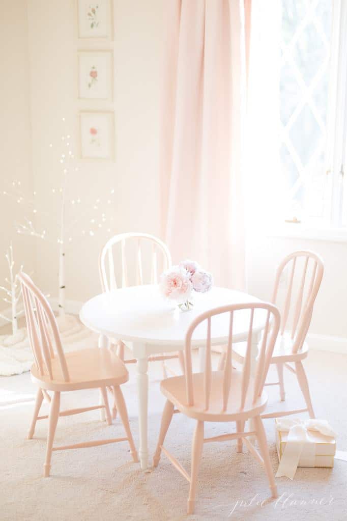 A white feminine bedroom with blush pink table and chairs, Christmas decorations added throughout the space.