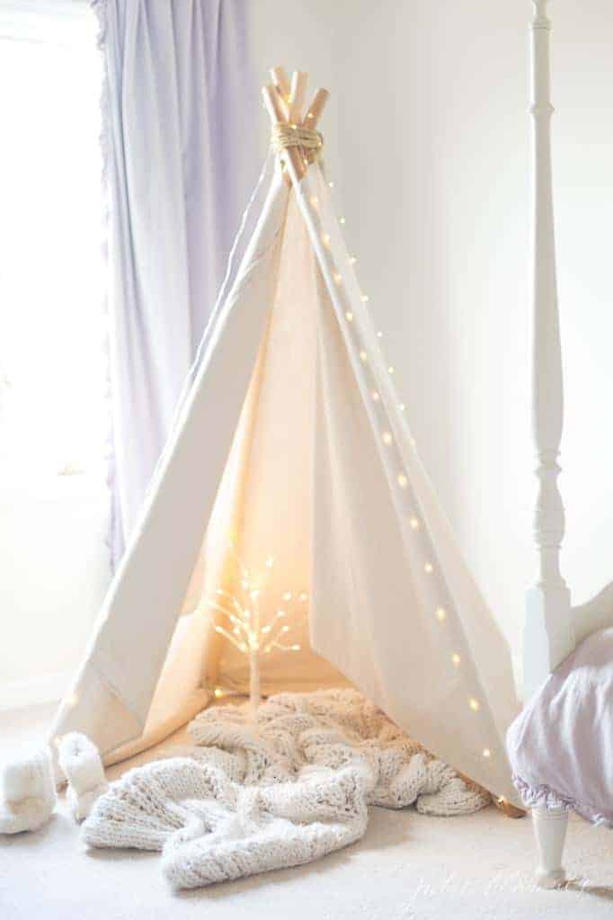 A white teepee in a white bedroom with warm and cozy Christmas decorations added to the interior.