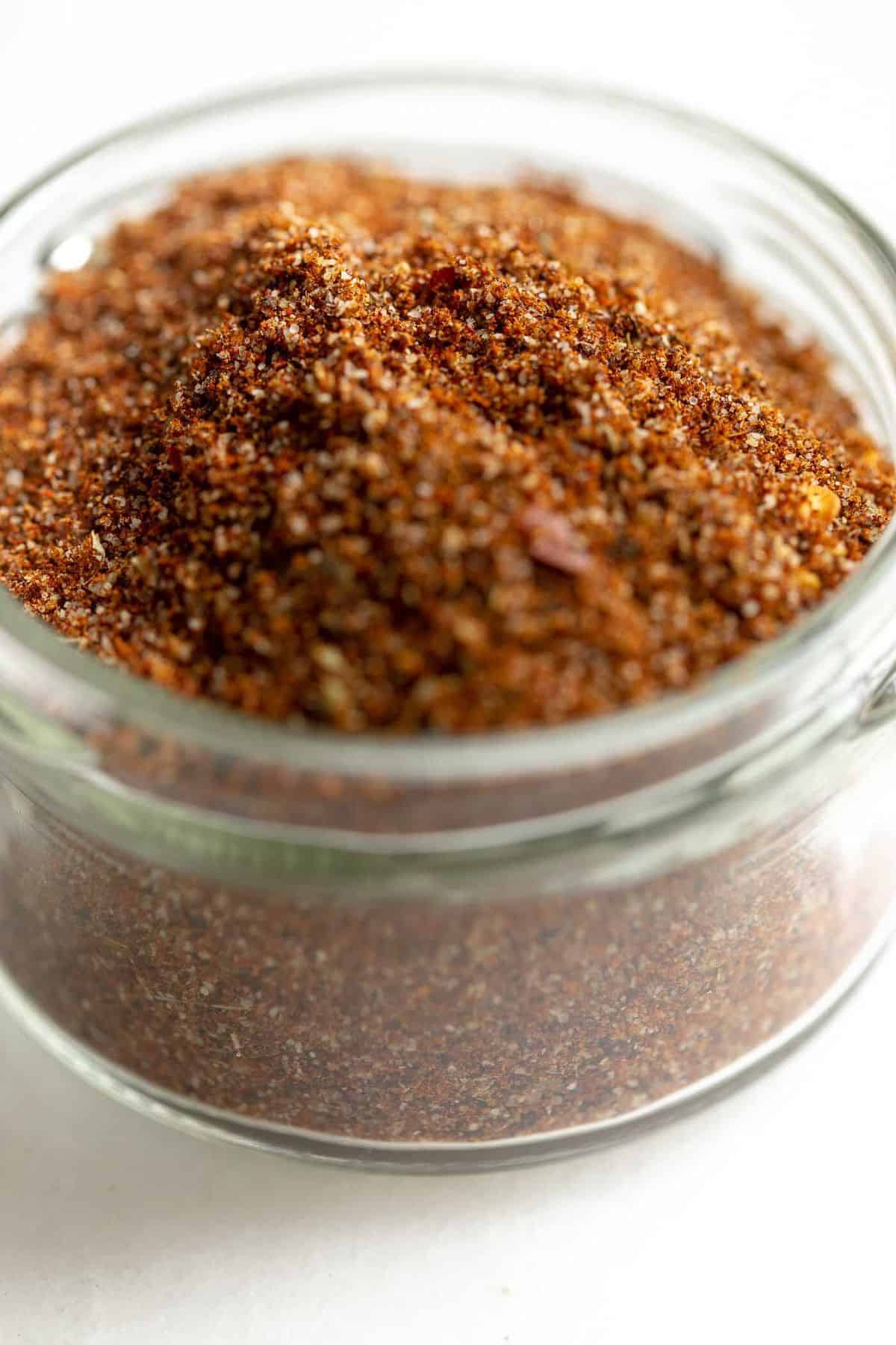 White counter top, small glass jar filled with spice mix, very close up..