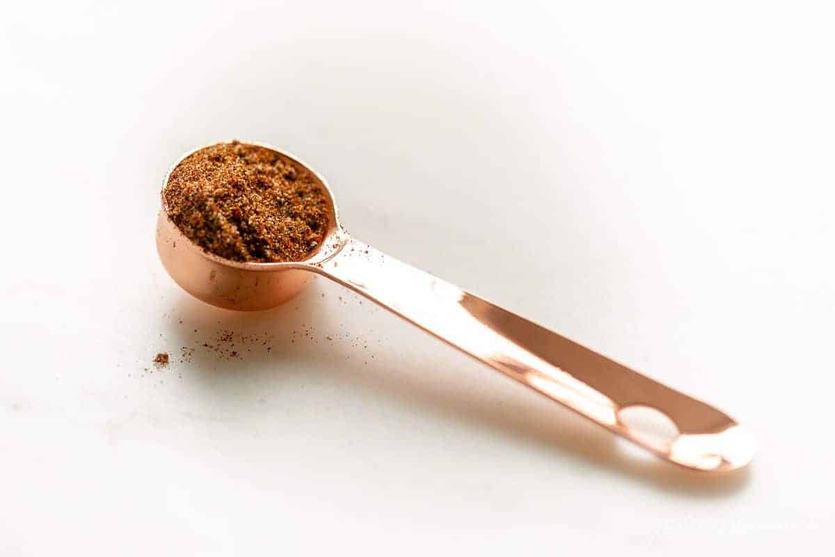 White surface, copper measuring spoon filled with Mexican easy seasoning recipe.