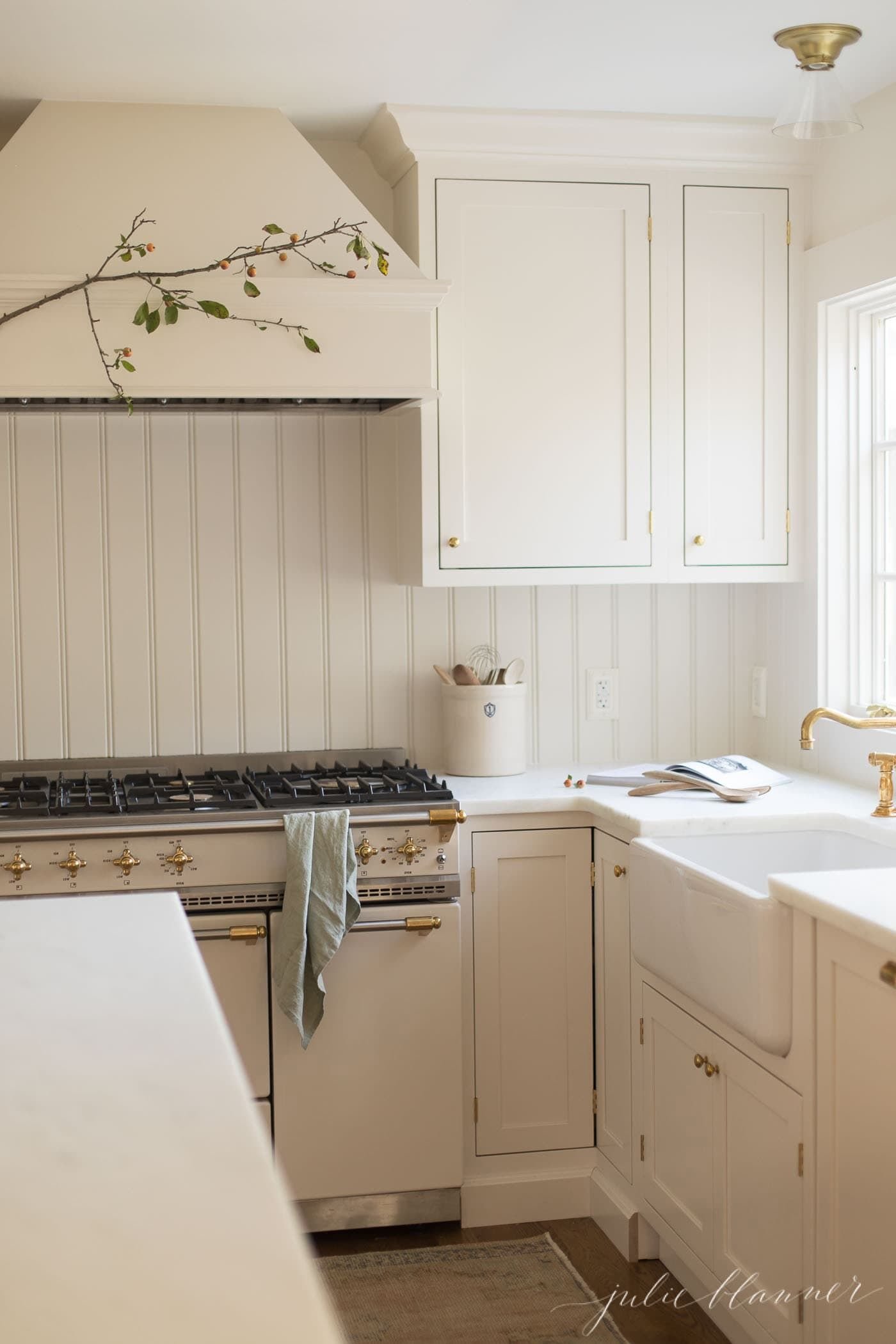 White kitchen cabinets with a fall branch on the range hood.