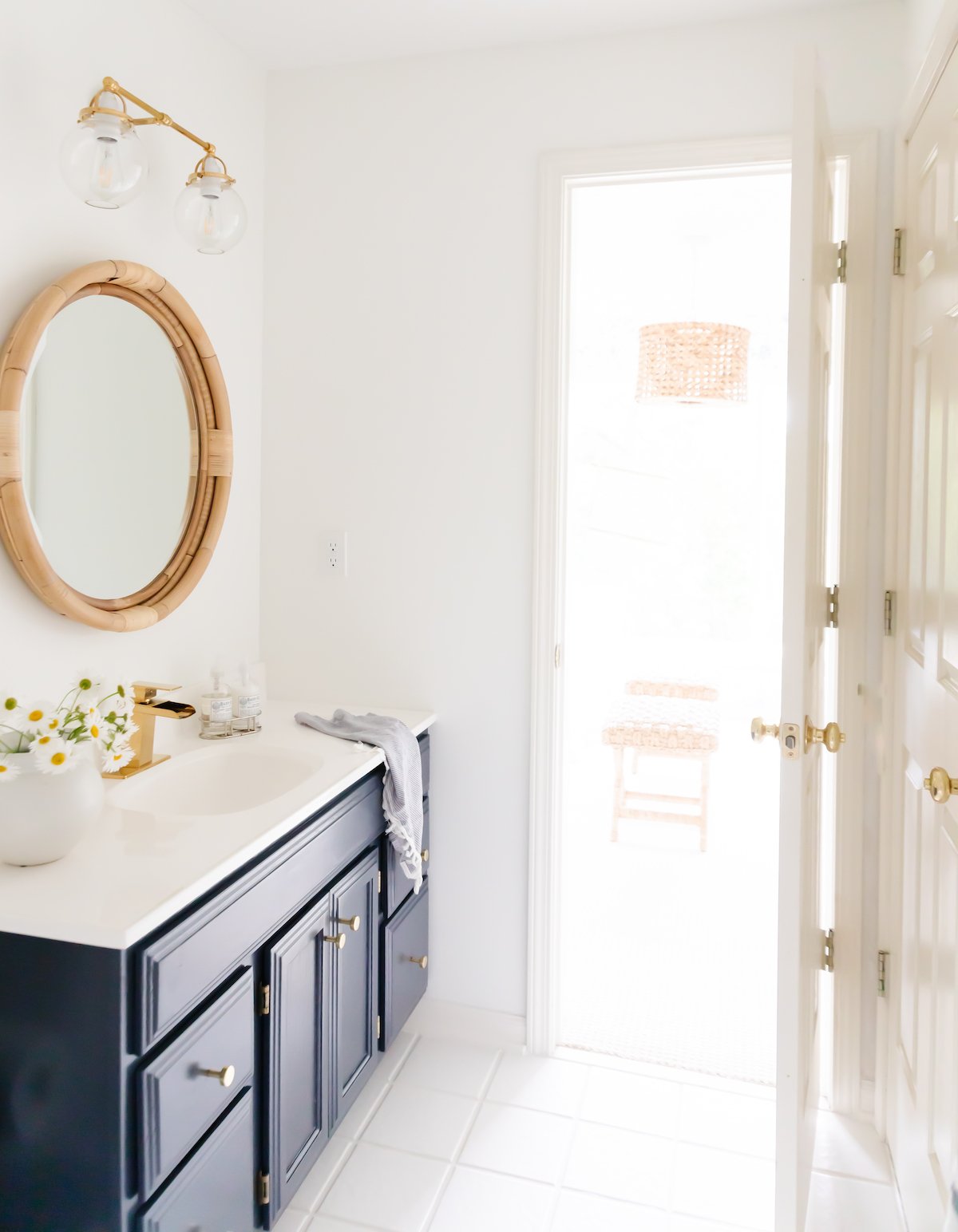 A white bathroom with a navy vanity and white tile floors with white grout paint.