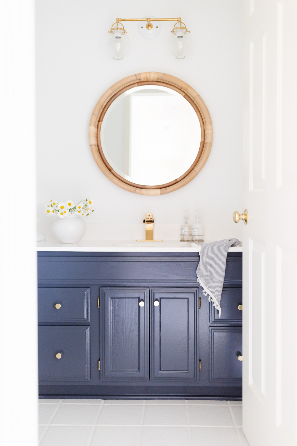 A white bathroom with a navy vanity and white tile floors with white grout paint.