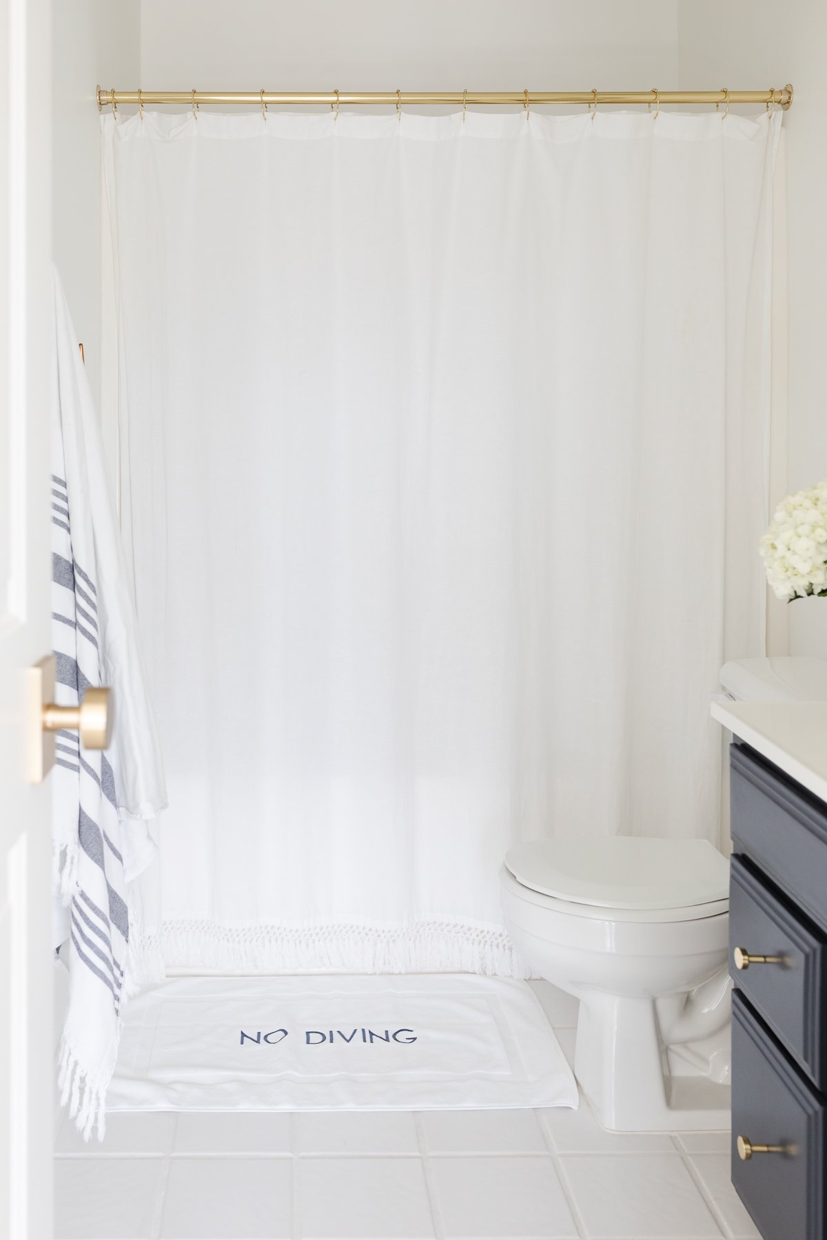 A white bathroom with a navy vanity and white tile floors with white grout paint.