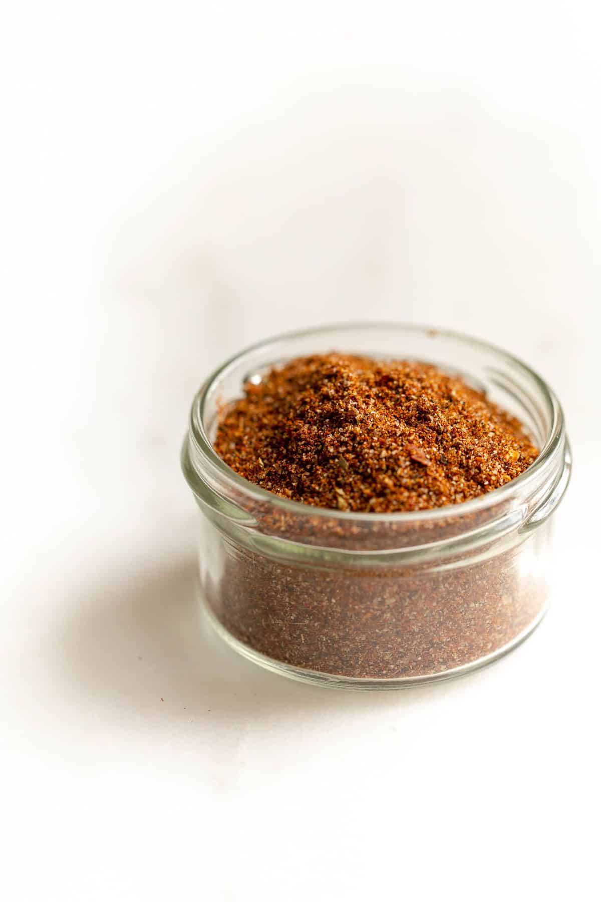 Homemade taco seasoning in a glass jar on a white surface.