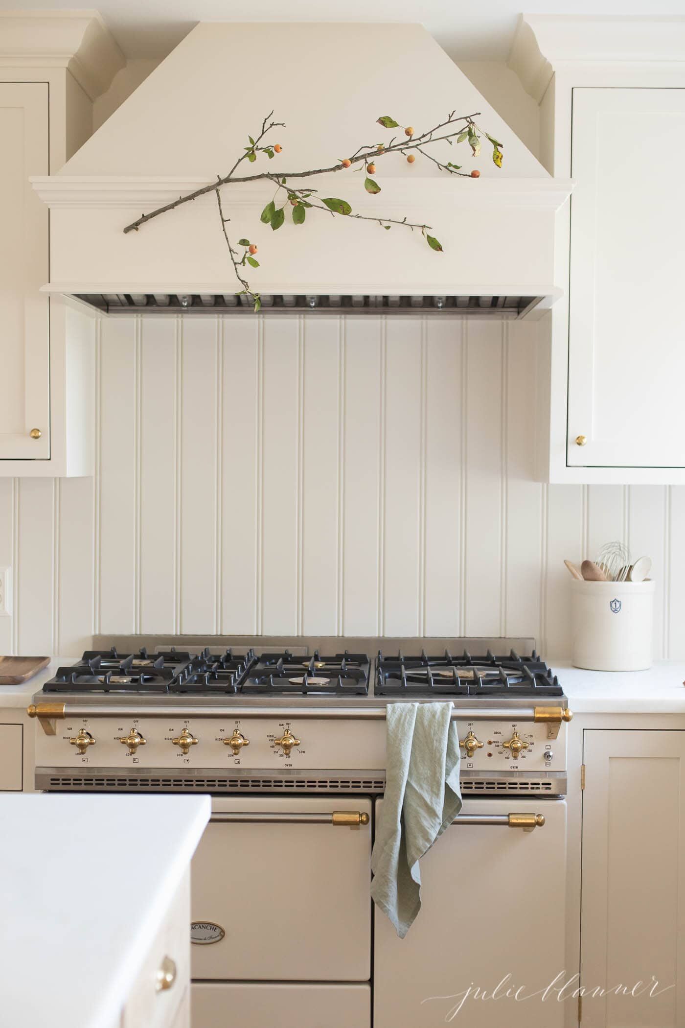 White kitchen cabinets with a fall branch on the range hood.