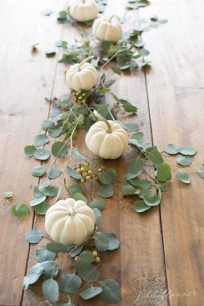 Rustic wooden table with white pumpkins and seeded eucalyptus down the center.