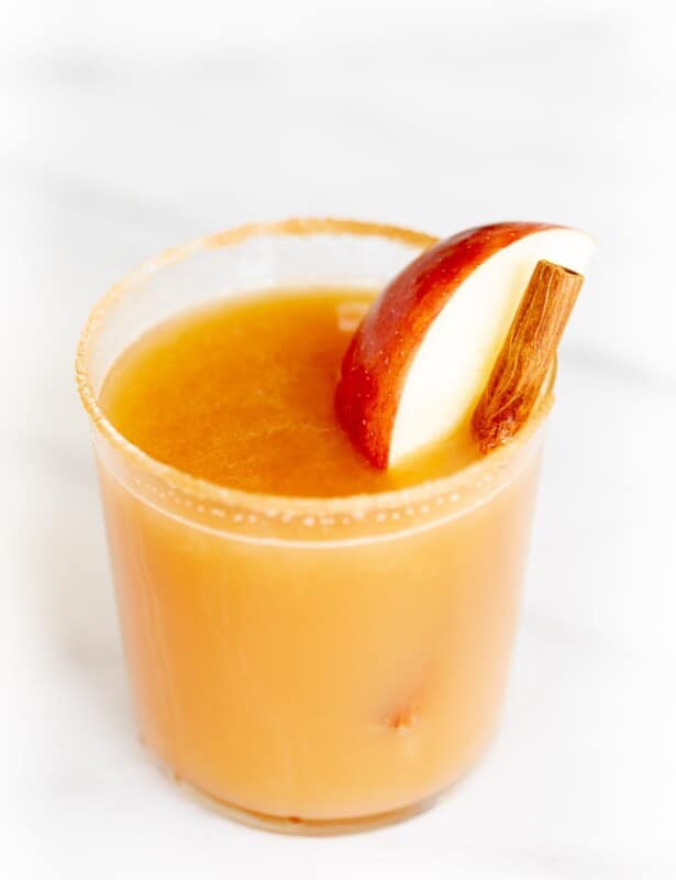 Cinnamon liquor cocktail glass on marble surface, garnished with apple slice and cinnamon sticks.