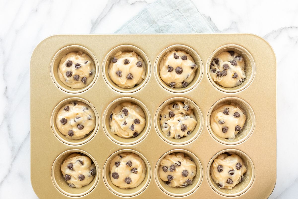 A gold mini muffin tin full of batter for a chocolate chip muffin recipe.