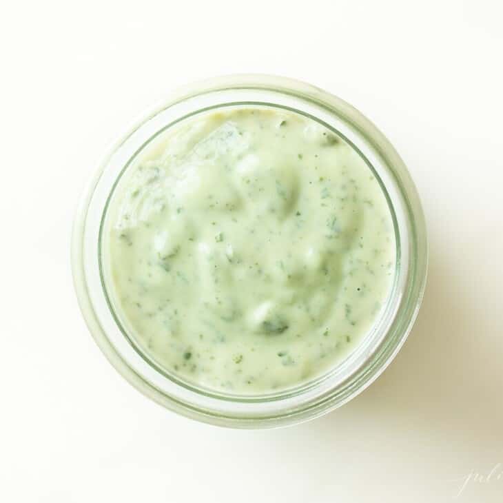 White surface with a small clear jar of pesto mayo.
