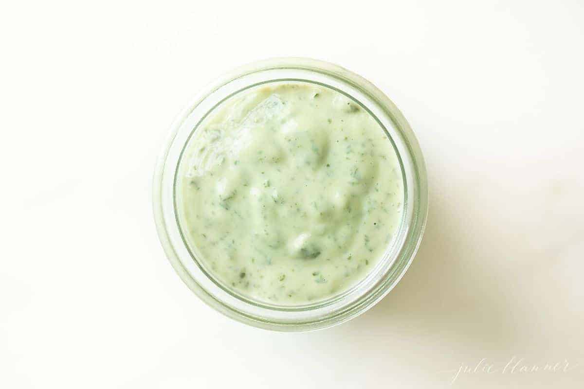 Pesto aioli in a glass jar on a white surface.