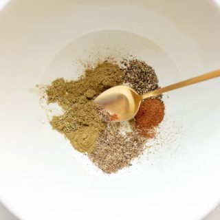 White bowl with poultry seasoning mix, gold spoon stirring.