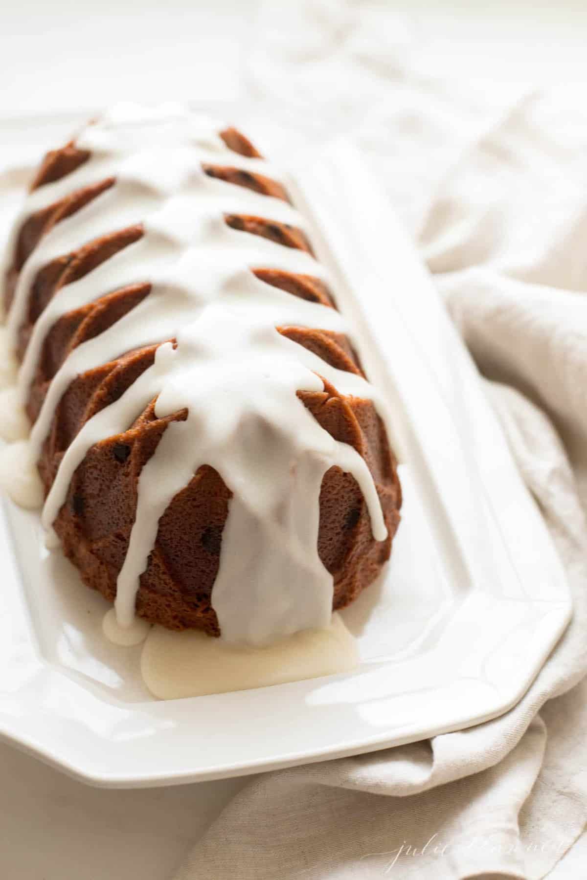 White tray with a dark cake loaf resting on top, glaze dripping onto surface.
