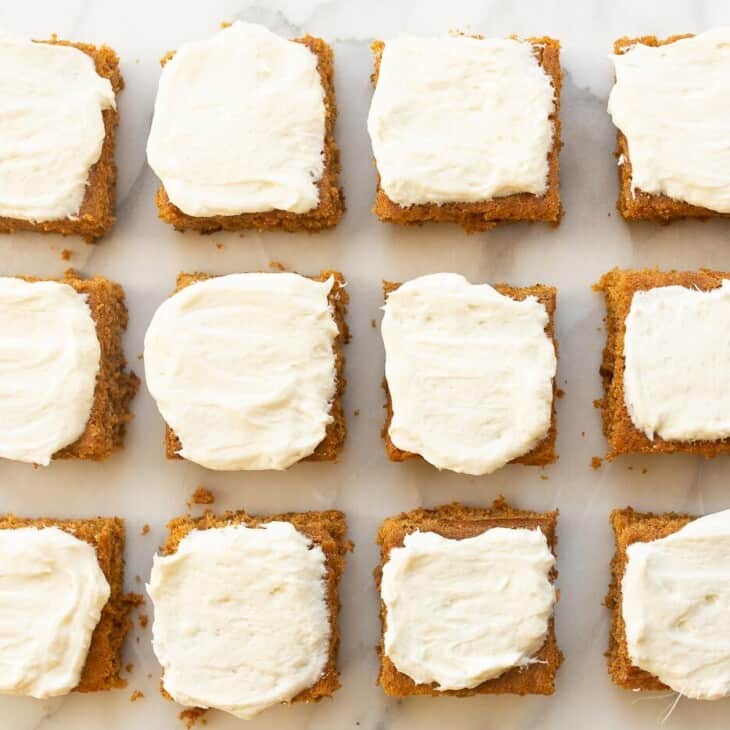 White surface with 12 cut pumpkin squares covered in frosting.
