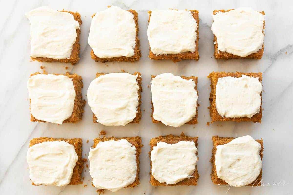 White surface with 12 cut pumpkin squares covered in frosting. 