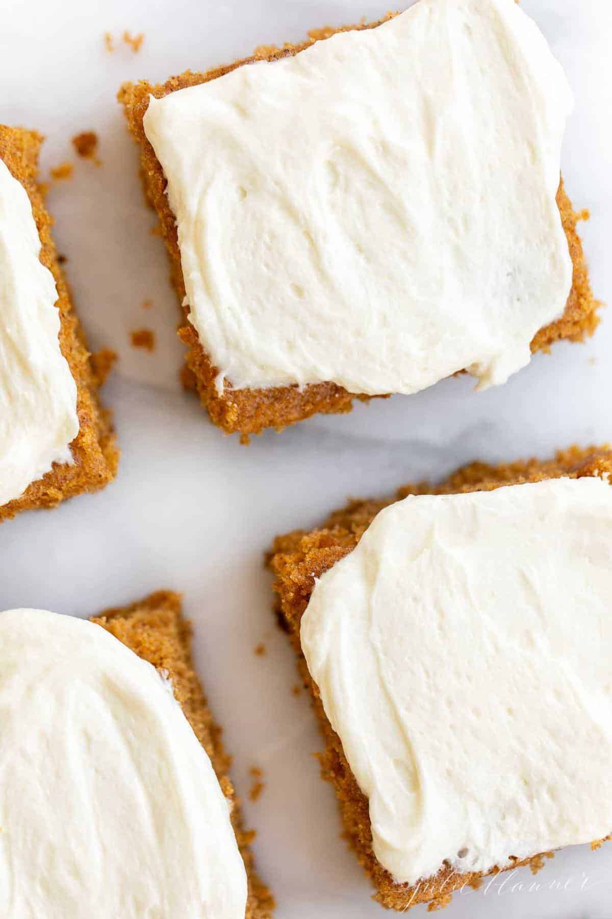 Cut pumpkin bars iced with cream cheese frosting on a marble surface. 