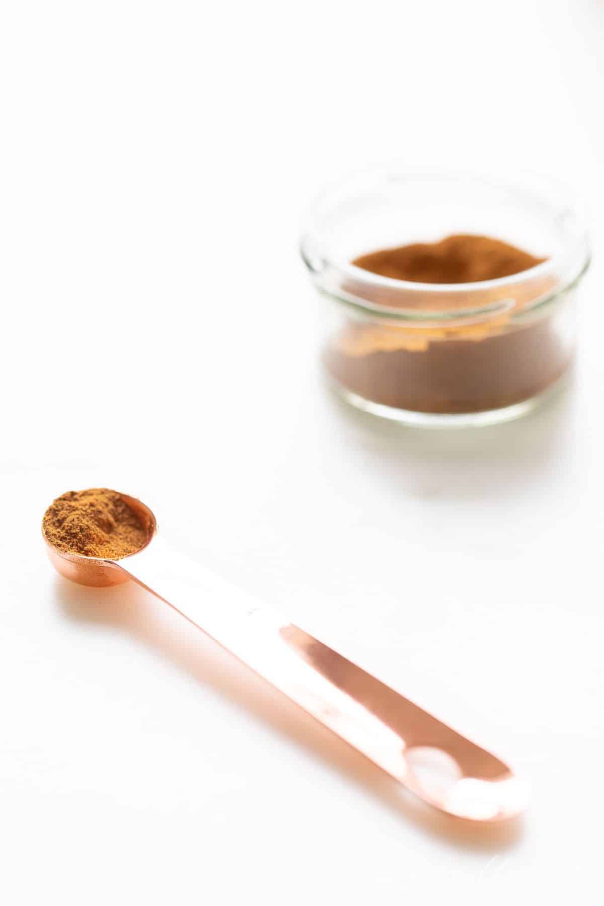 Pumpkin pie spice in a measuring spoon and in a glass jar to the side. 