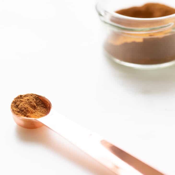 Small glass jar filled with spice mix on a white surface, teaspoon in foreground.