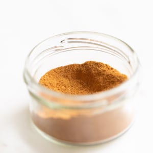 A small clear jar of pumpkin pie spice on a white countertop.