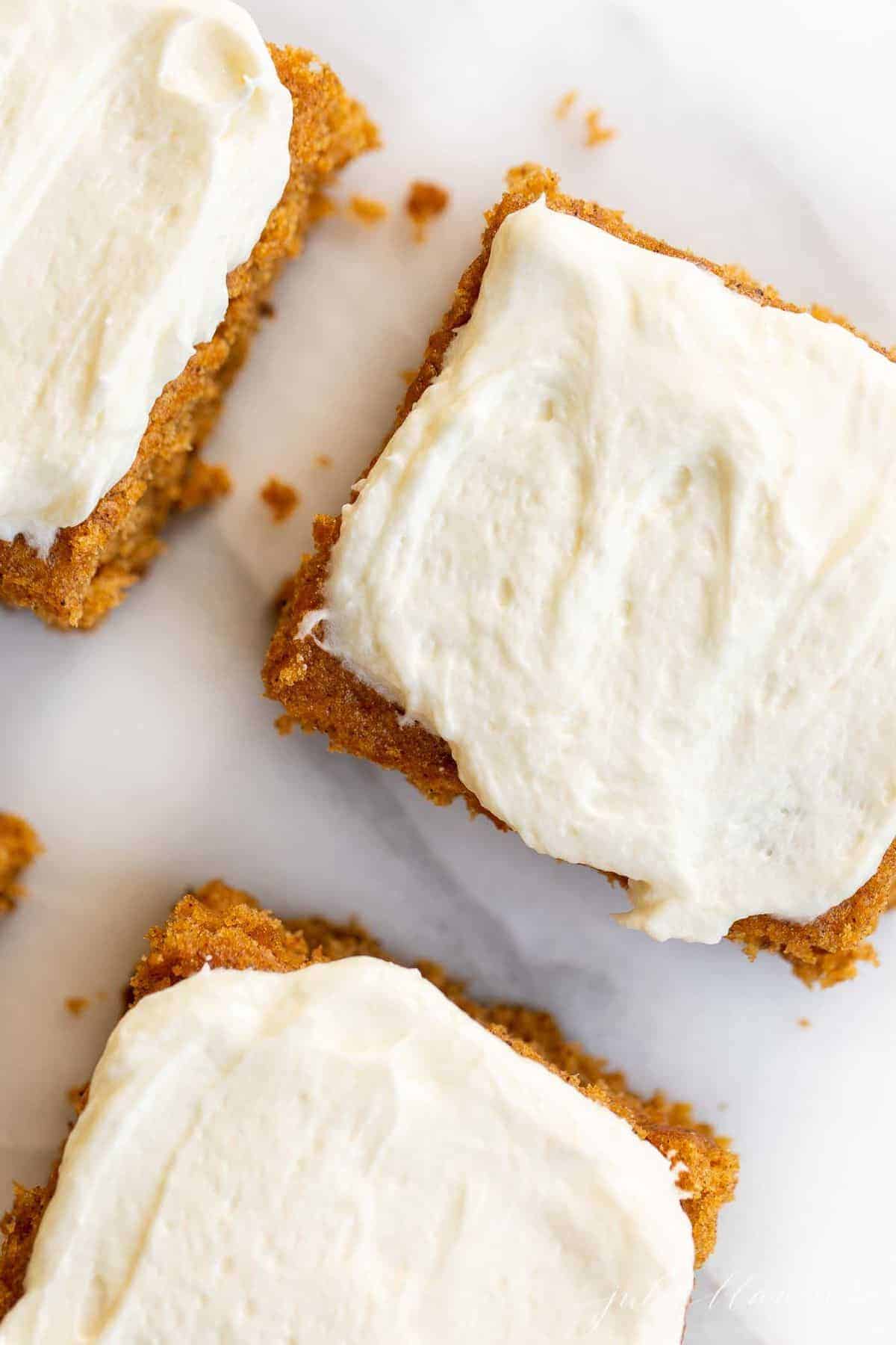 White marble surface with a close up of pumpkin bars cut and covered in cream cheese frosting.