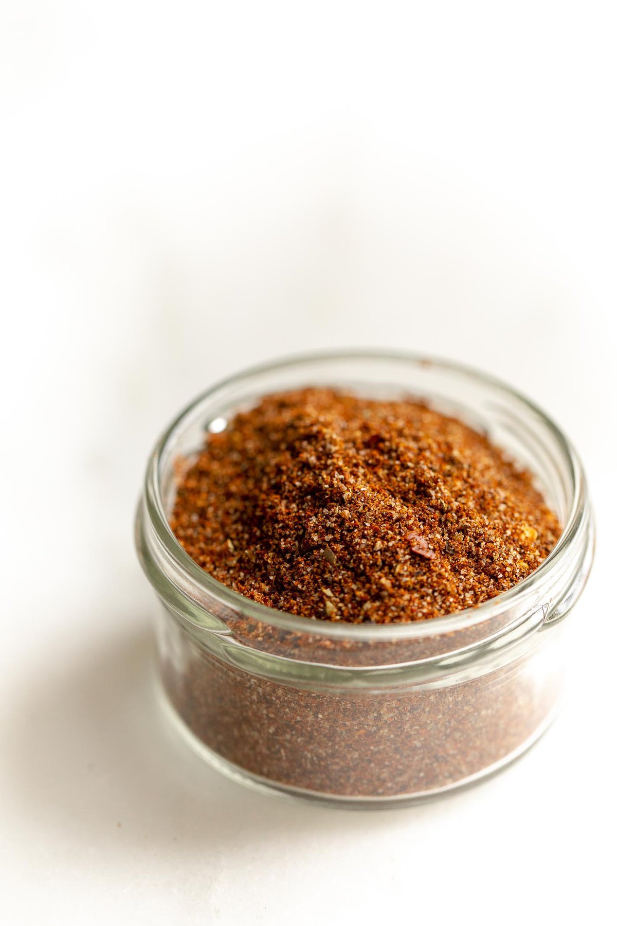 A small glass jar full of taco seasoning on a marble countertop.