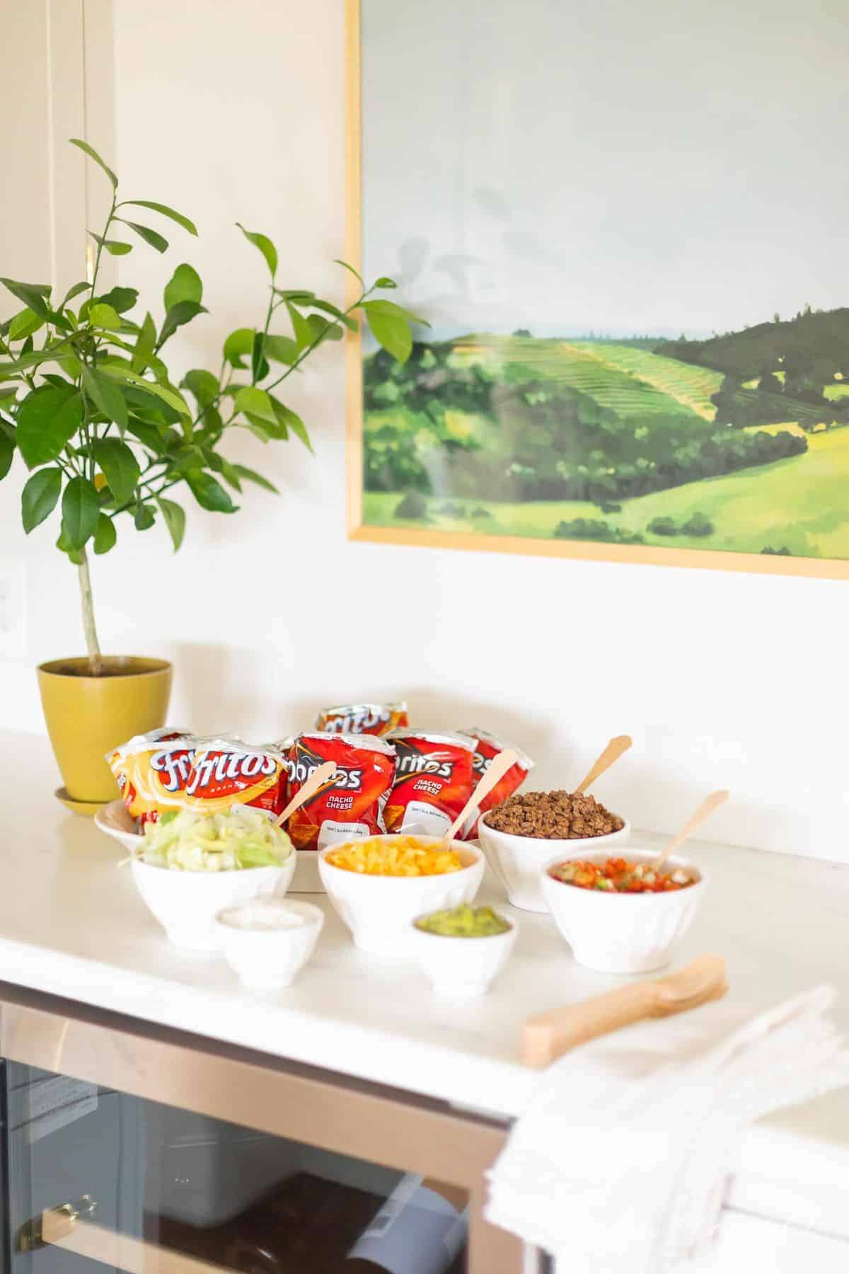 Walking taco bar display with chips and various toppings in white bowls.