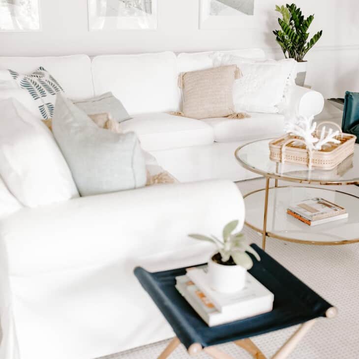 White living room with white sofa, glass coffee table and pair of navy blue chairs.